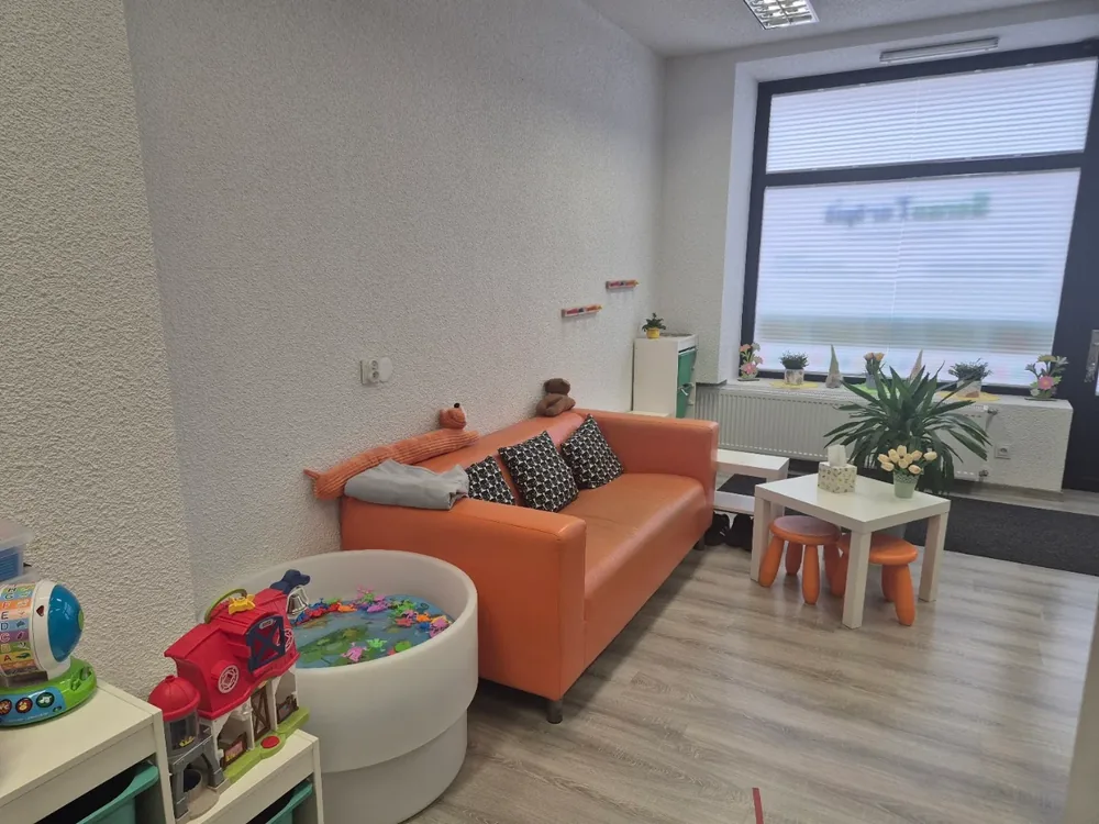 Wnętrze gabinetu z pomarańczową kanapą, stolikiem i zabawkami